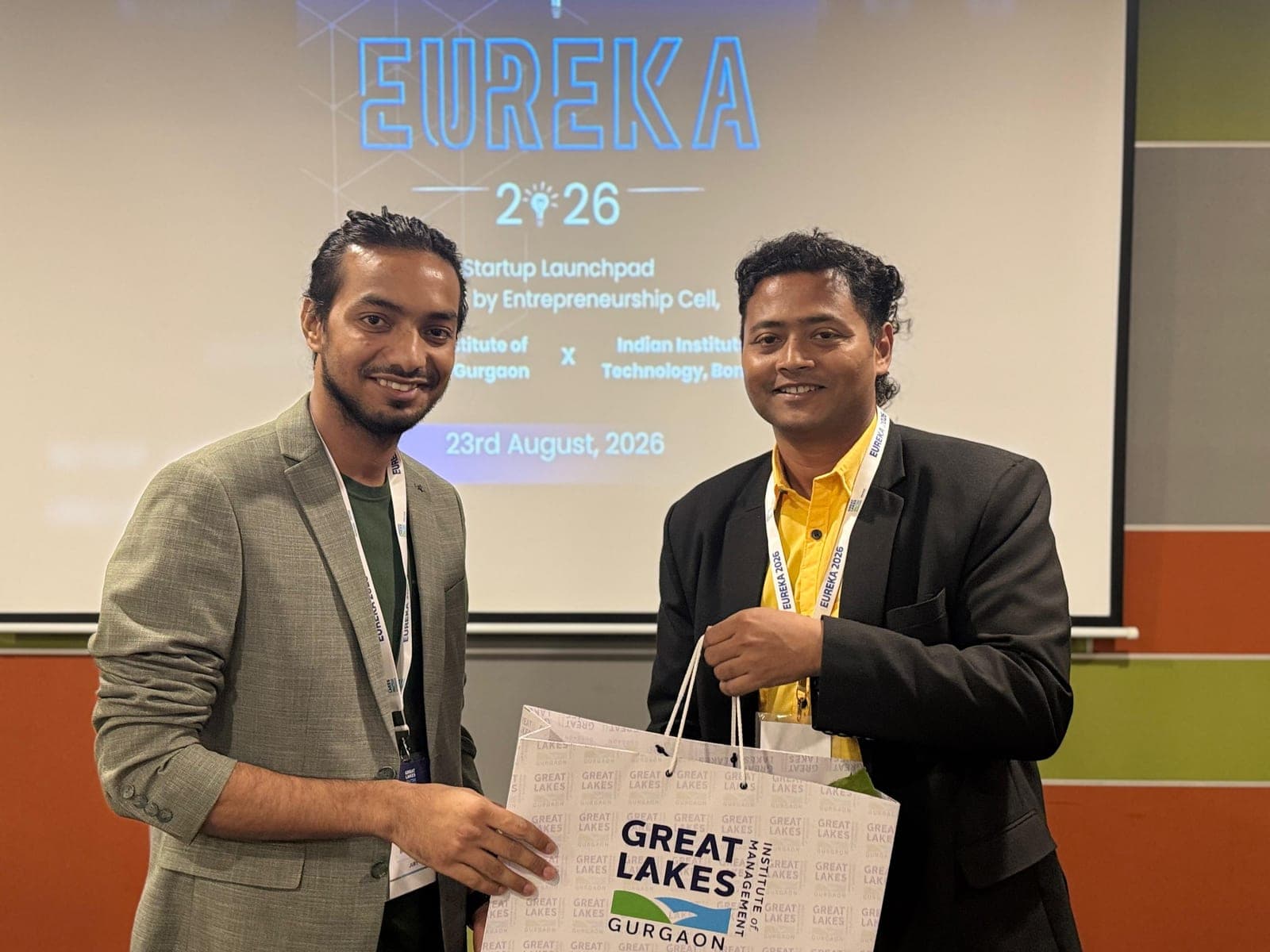 Dr Swapnil Sahoo with a fellow organizer, both holding a Great Lakes Gurgaon gift bag, in front of the EUREKA 2026 screen