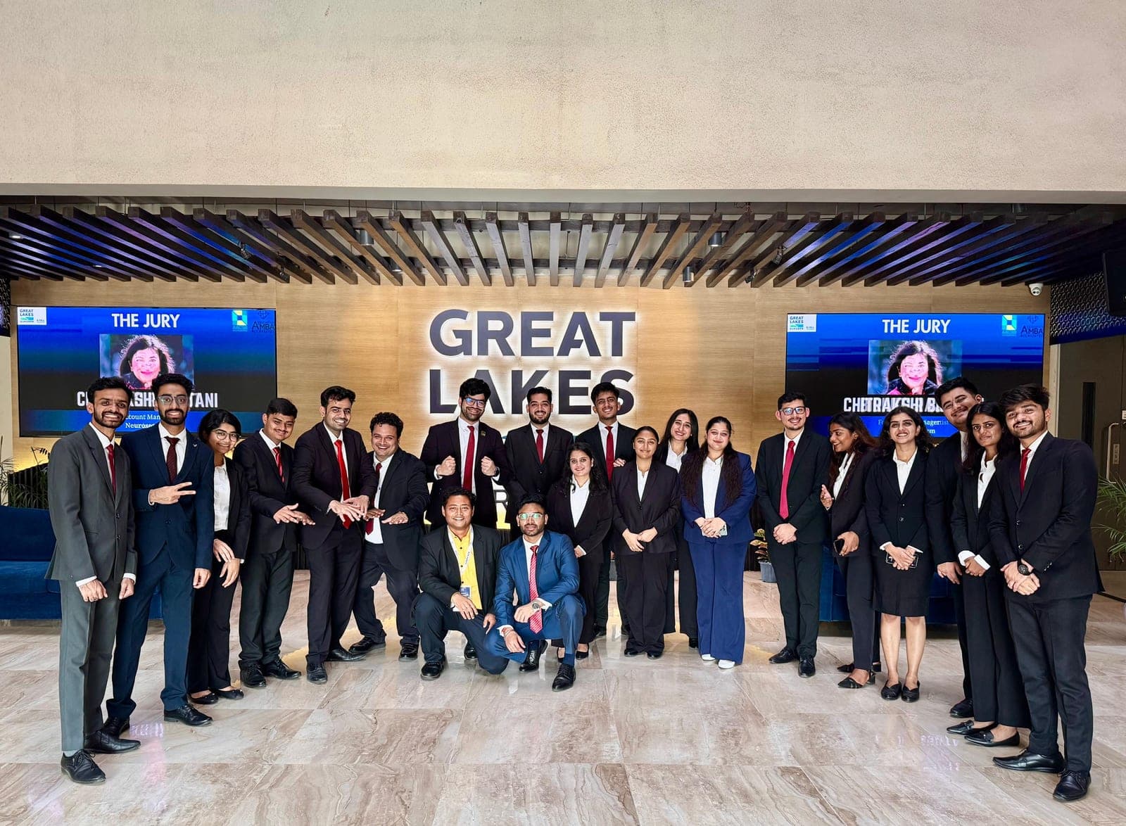 The EUREKA 2026 organizing team posing in the Great Lakes Gurgaon lobby, with jury panel introductions displayed on screens behind them